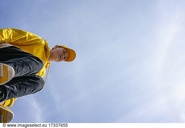 Vorpubertärer Junge mit gelbem Sweatshirt und Mütze an einem sonnigen Tag