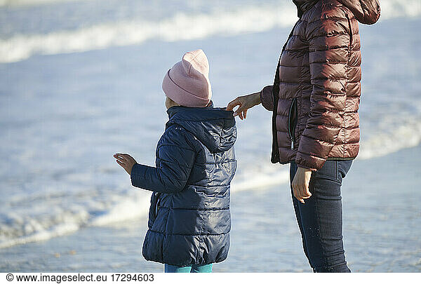 Vorsichtiges Festhalten der Tochter an der Kapuze am Strand