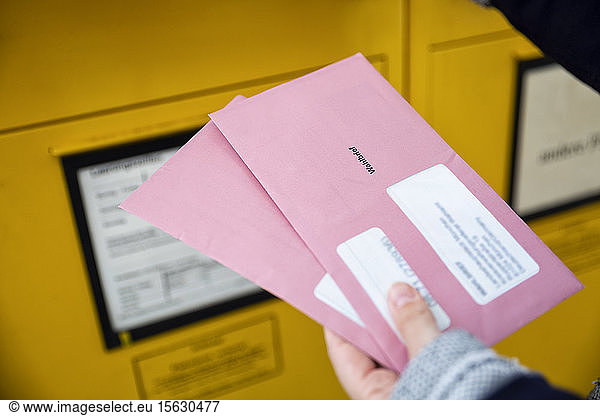 Wähler  der Dokumente für die Briefwahl vor den Briefkasten hält