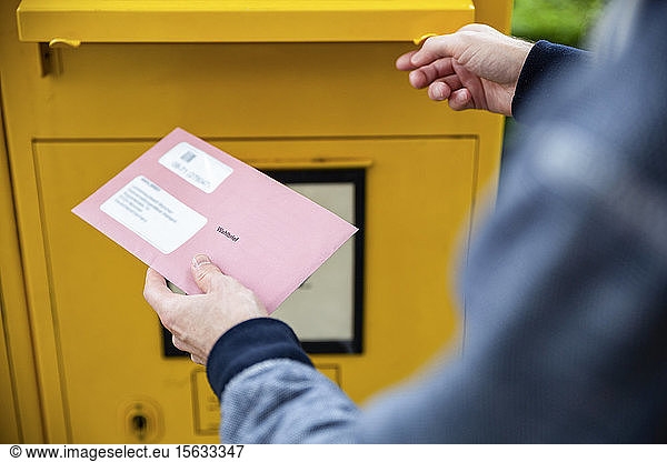 Wähler  der Dokumente für die Briefwahl vor den Briefkasten hält