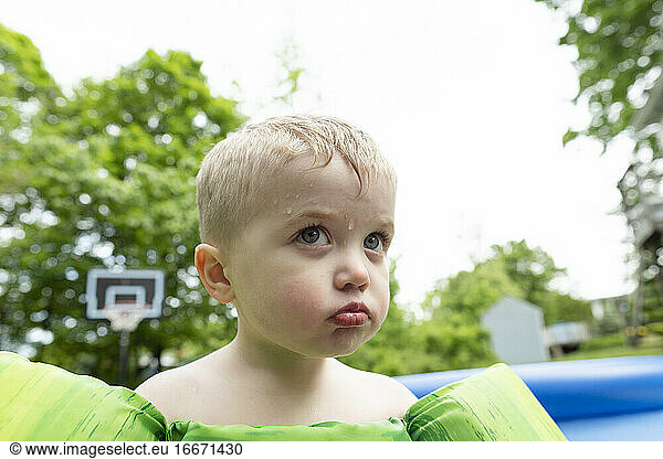 Wütendes Kind schmollt neben dem Schwimmbad  während Wasser auf sein Gesicht tropft