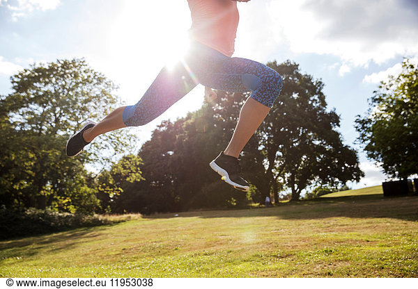 Waist down view of young woman training in park  leaping mid air in sunlight