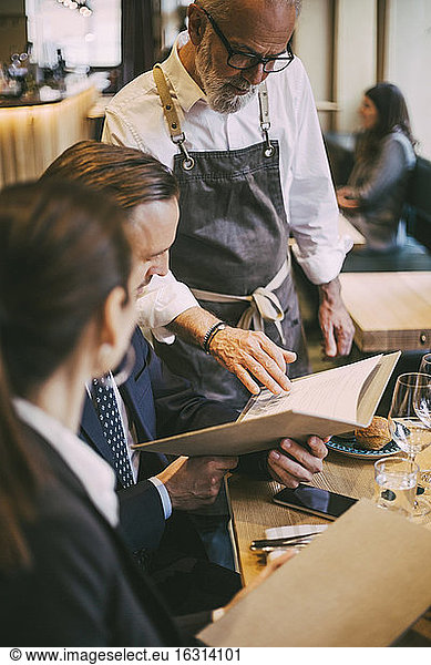 Waiter standing by table while business professionals sitting in restaurant