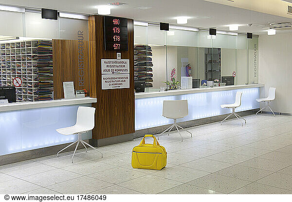 Waiting area and reception desk at a modern hospital  with signs and electronic display Yellow bag.
