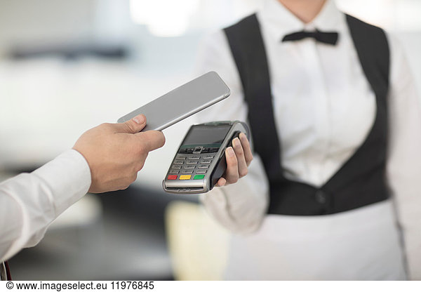 Waitress holding payment machine toward customer  customer paying by contactless method