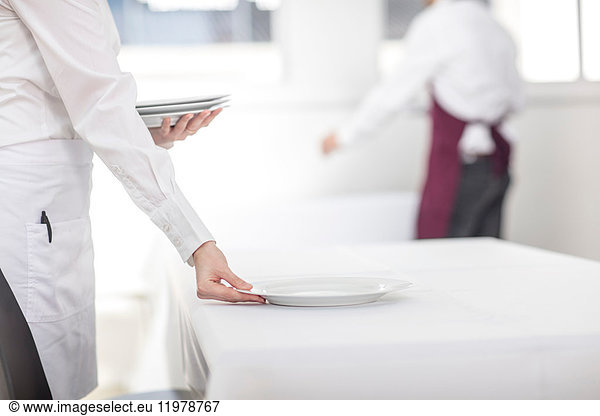 Waitress laying table in restaurant  mid section