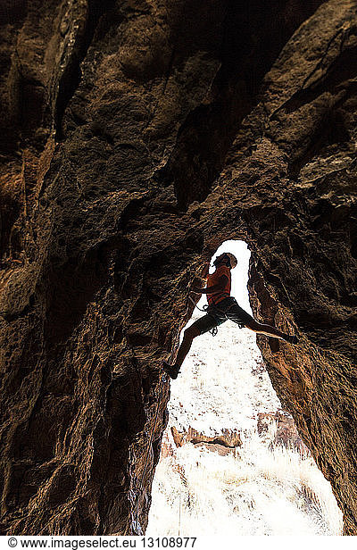 Wanderer beim Klettern in einer Höhle in der Wüste an einer Felsformation festhalten