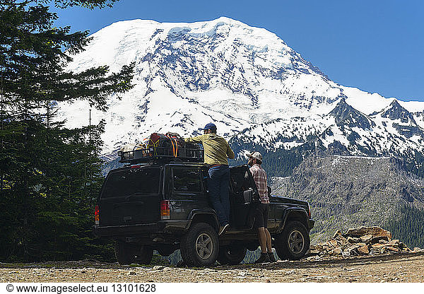 Wanderer  der Gepäck im Geländewagen von einem Freund gegen schneebedeckte Berge anpasst