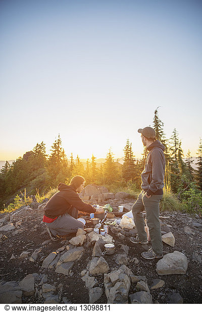 Wanderer  die bei Sonnenuntergang am Berg vor klarem Himmel Essen zubereiten