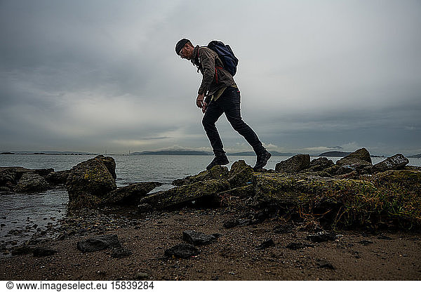 Wanderer geht über moosbewachsene Schlammsteine vom Bauwerk am Strand der Bucht