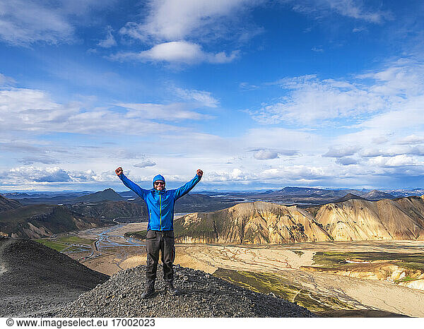 Wanderer posiert mit erhobenen Armen auf einem vulkanischen Hügel in Landmannalaugar
