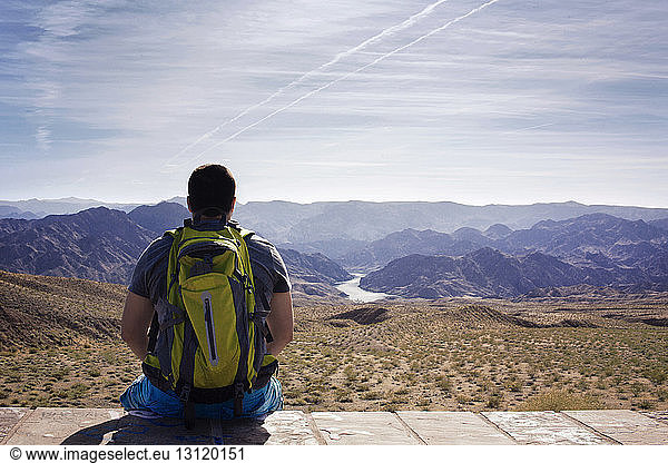 Wanderer schaut auf Berge  während er auf Stützmauer sitzt