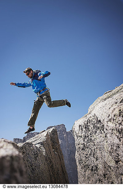 Wanderer springt auf Felsformationen vor klarem blauen Himmel