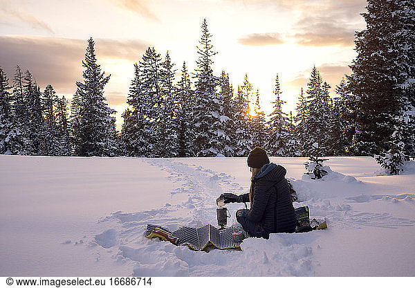 Wanderin bei der Essenszubereitung auf schneebedecktem Land bei Sonnenuntergang