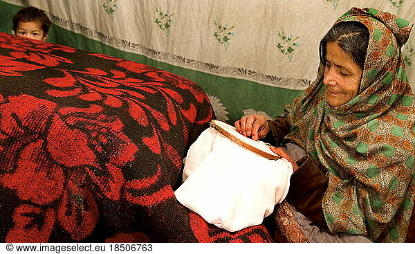 War widow works on embroidery while her grandchild looks on.