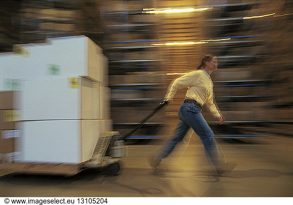 Warehouse employee moving a pallet of products in cardboard boxes in a large distribution warehouse.