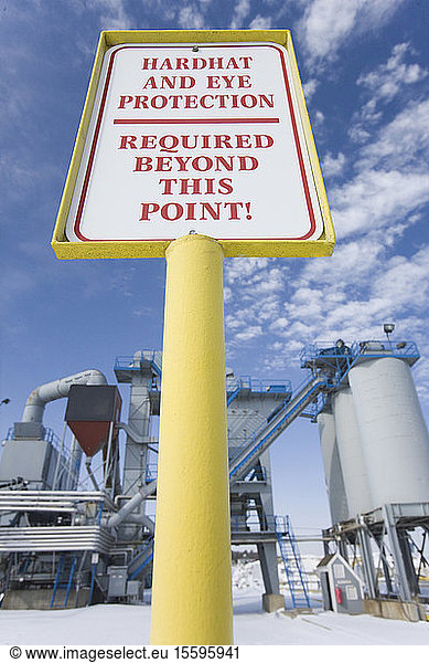 Warning sign saying 'Hardhat and Eye Protection Required Beyond This Point' at an asphalt plant