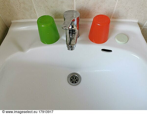 Waschbecken mit bunten Zahnputzbechern aus Plastik und einem Seifenstück in einem primitiven Hotel
