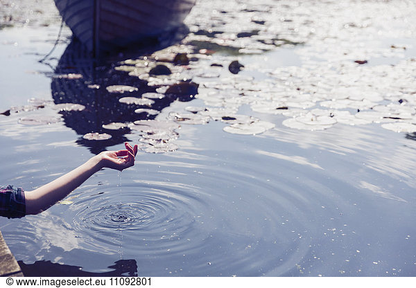 Wasser tropft aus der Hand der Frau am sonnigen See mit Seerosenblättern