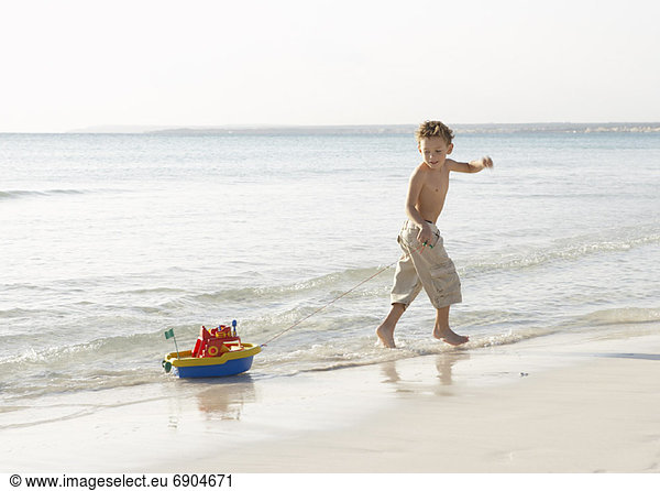Wasserrand ziehen Junge - Person Spielzeug Boot vorwärts