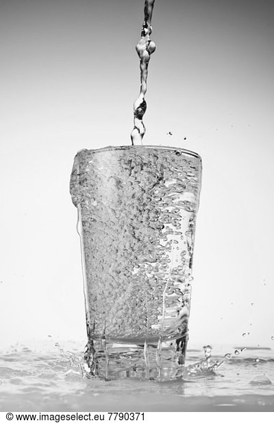Water being poured into drinking glass and overflowing