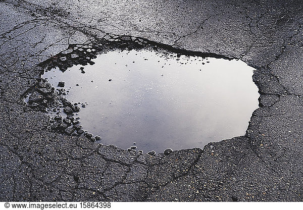 Water filled pothole on urban street with cracks and fracture marks