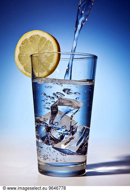 Water is poured into a glass with ice cubes and lemon slice