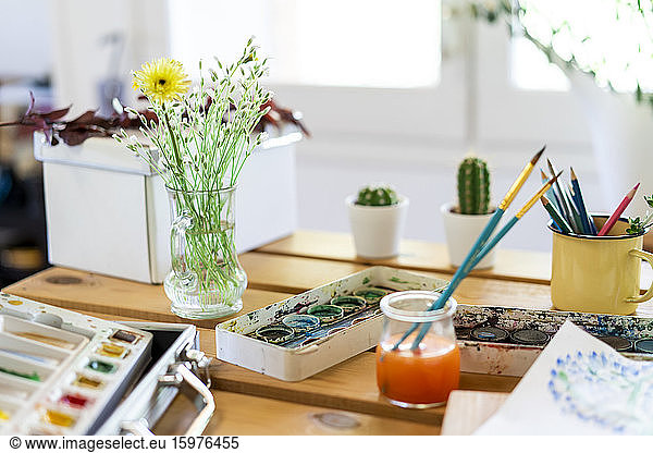 Watercolor paints with flower vase and paintbrushes on wooden table home