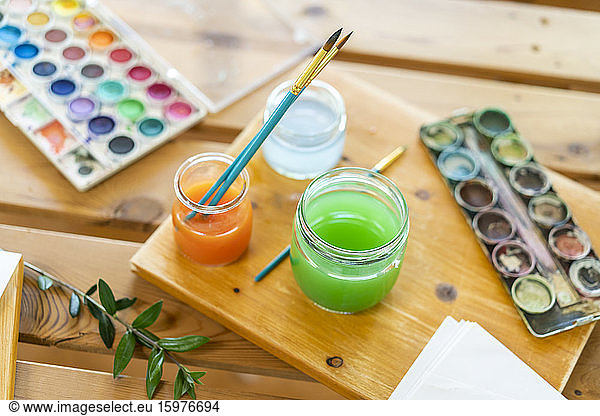 Watercolor paints with water and paintbrushes on wooden table home