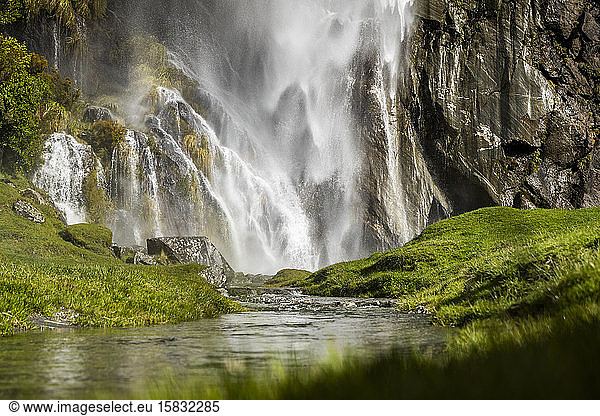 Waterfall cascading over rocks in a lush green grassy nature landscape