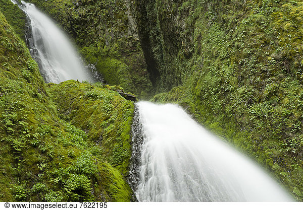 Waterfall rushing over green rocky hillside