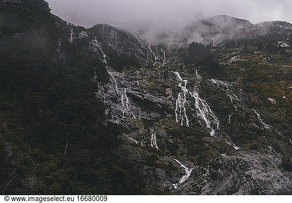 Waterfalls down a mountain into Milford Sound  foggy and rainy day  NZ