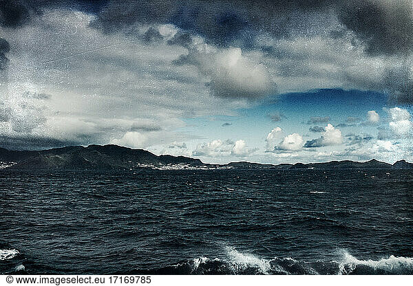 Waves splashing in sea against cloudy sky