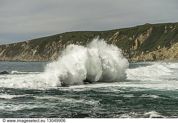 Waves splashing on rocks in sea against sky