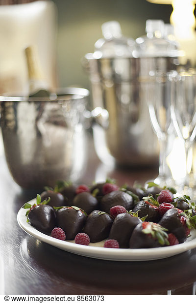 Wedding dessert. Plate of hand-dipped organic strawberries,  fruit in artisinal handmade chocolate with raspberry garnish. Champagne and glasses.