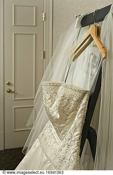 Wedding dress and veil hanging on rack in hotel room.