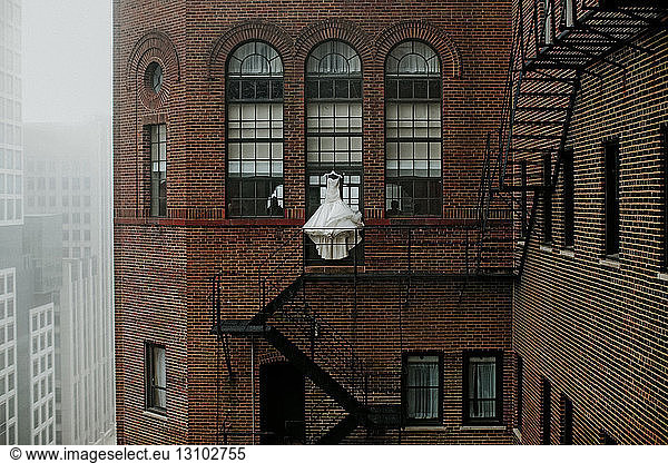 Wedding dress hanging by fire escape of building in city
