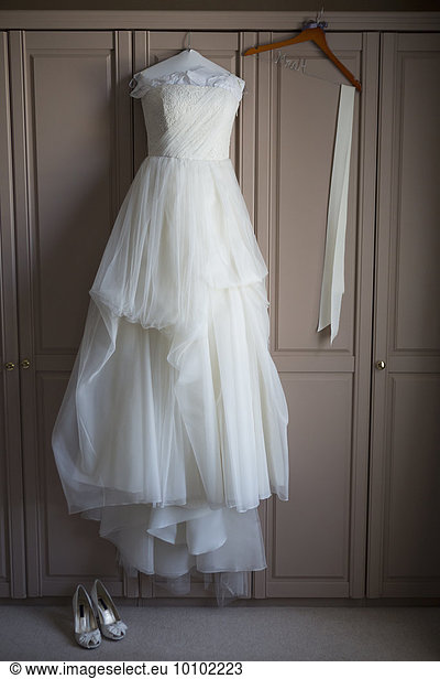 Wedding dress hanging on a wardrobe door wedding shoes on the floor.