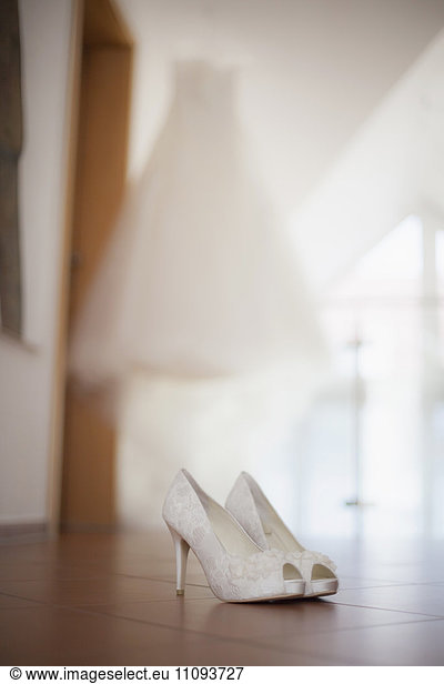 Wedding shoes on the floor with wedding dress in background