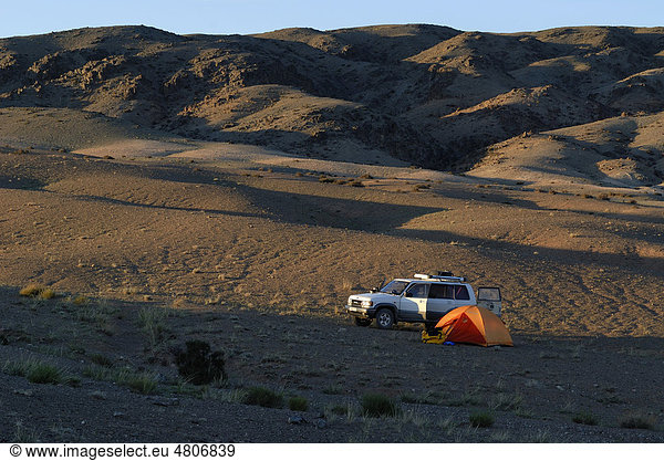Weißer Opel Landcruiser steht im letzten Abendlicht neben Zeltlager mit Trekkingzelt und Outdoor Equipment in der Wüste Gobi  Khorgoryn Els  Gurvan Saikhan Nationalpark  Ömnögov Aimak  Mongolei  Asien