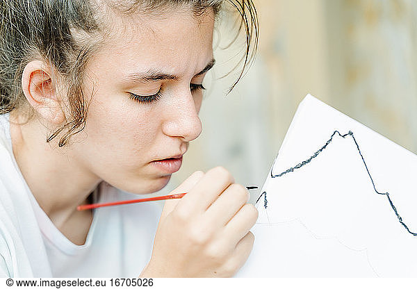 weißes Mädchen malt mit einem Pinsel ihr Bild beginnend mit schwarzem Pinselstrich. Horizontal Foto
