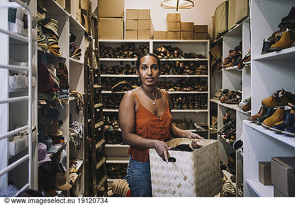 Weibliche Angestellte  die einen Weidenkorb trägt  während sie inmitten von Schuhregalen im Geschäft steht