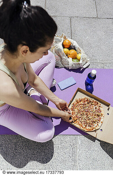 Weibliche Athletin isst Pizza auf einer Trainingsmatte an einem sonnigen Tag