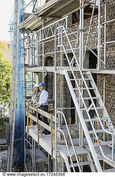 Weibliche Bauherrin zeigt einem männlichen Architekten die Konstruktion  während sie auf dem Balkon der Baustelle steht