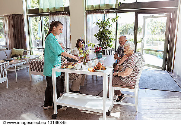 Weibliche Betreuerin serviert älteren Menschen im Pflegeheim Frühstück