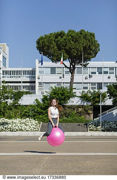Weibliche Fachkraft hüpft mit Ball auf der Straße an einem sonnigen Tag