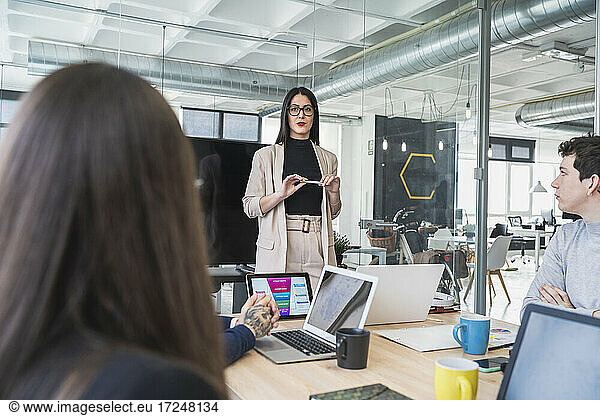 Weibliche Fachkraft im Gespräch mit männlichen und weiblichen Unternehmern während eines Treffens im Coworking-Büro
