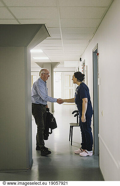 Weibliche Krankenschwester beim Händeschütteln mit einem männlichen älteren Patienten auf dem Flur eines Krankenhauses