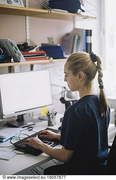 Weibliche Krankenschwester mit Pferdeschwanz arbeitet am Computer  während sie am Schreibtisch in der Klinik sitzt