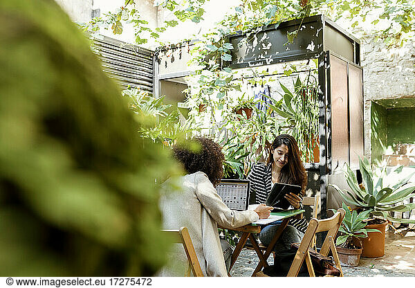 Weibliche Mitarbeiter  die an einem digitalen Tablet und einem Laptop arbeiten  während sie an einem sonnigen Tag in einem Café sitzen